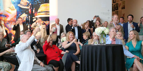 A group of standing and seated people raising their glasses in a toast